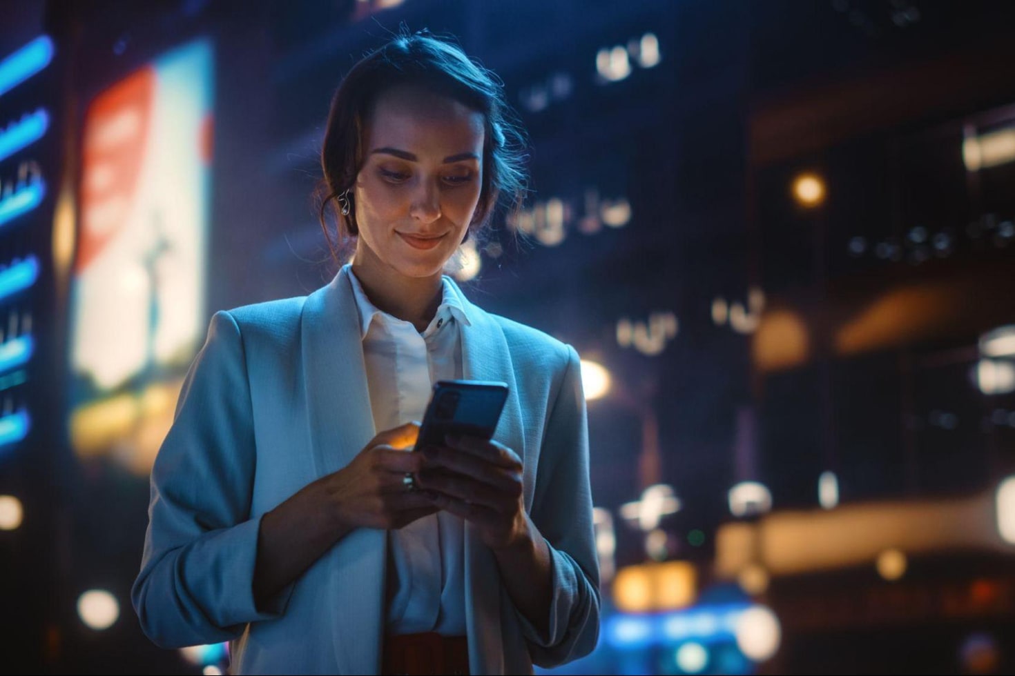 young woman in a city at night using smartphone